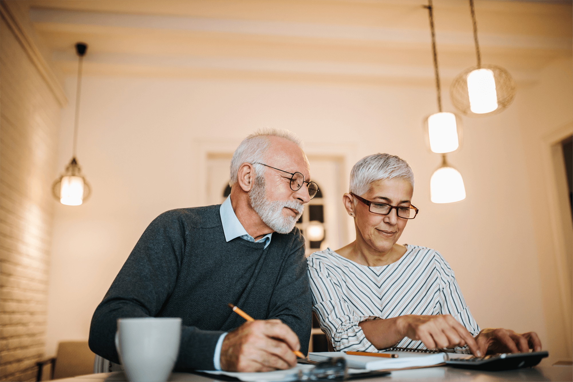 An elderly couple sit at table with a notebook and calculator.