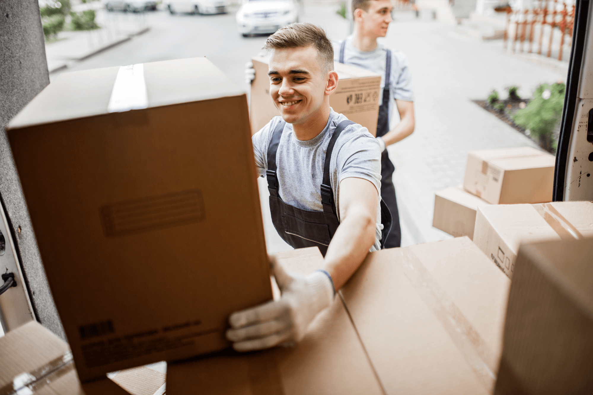 Two young men load cardboard boxes onto a van.