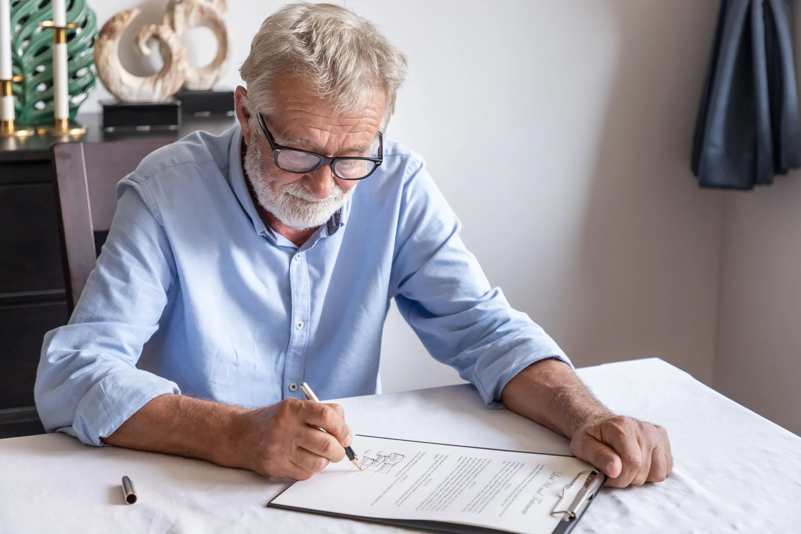 An elderly man sits at a table signing a document.