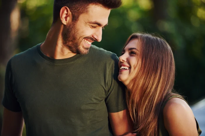 A couple take a walk outside laughing together whilst the woman has her head on the mans shoulder.