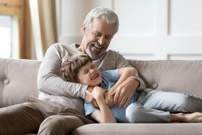 A grandad plays with his grandson on the sofa tickling him.