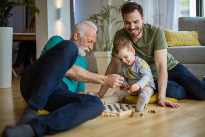 Grandpa will teach him the game of chess. Grandfather his adult son and grandson playing at home.