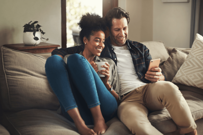 A couple sits on the sofa looking at a phone as one holds a mug.