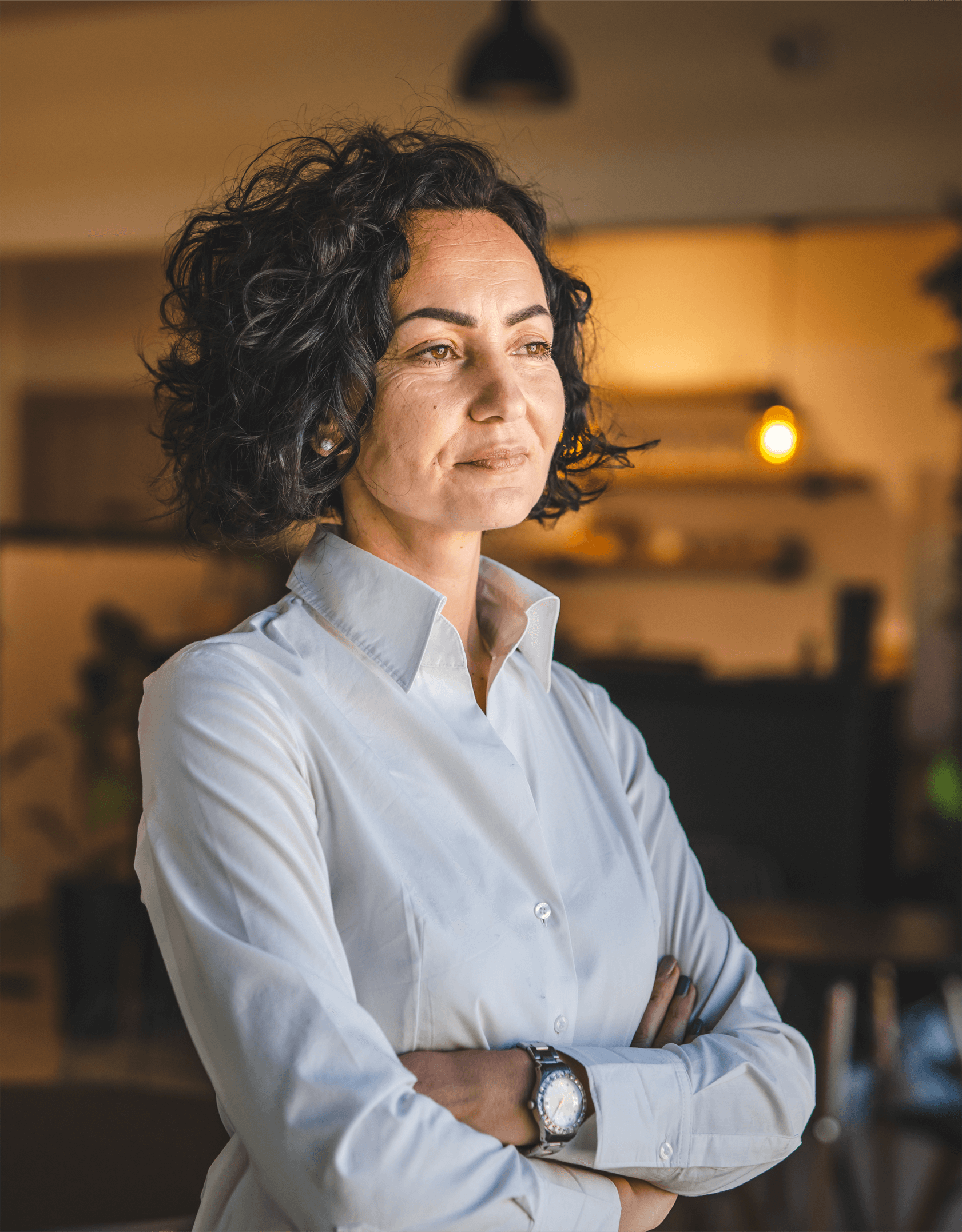 A woman stands with armed crossed looking into the distance.