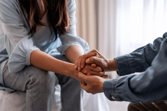 Two people sit opposite each other with their hands clasped.
