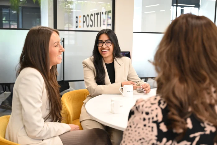 Three women sat at a table having a conversation and laughing.