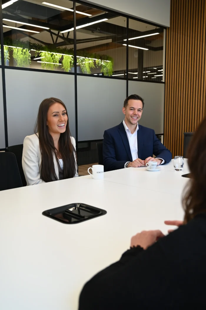 Lucy Cresswell and Russell Kaminski sit at a board room table talking to someone out of shot.