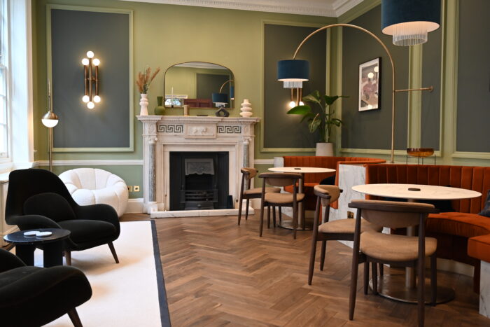 A period room modernly decorated with green walls and wooden floor with multiple seating areas and a marble fireplace.