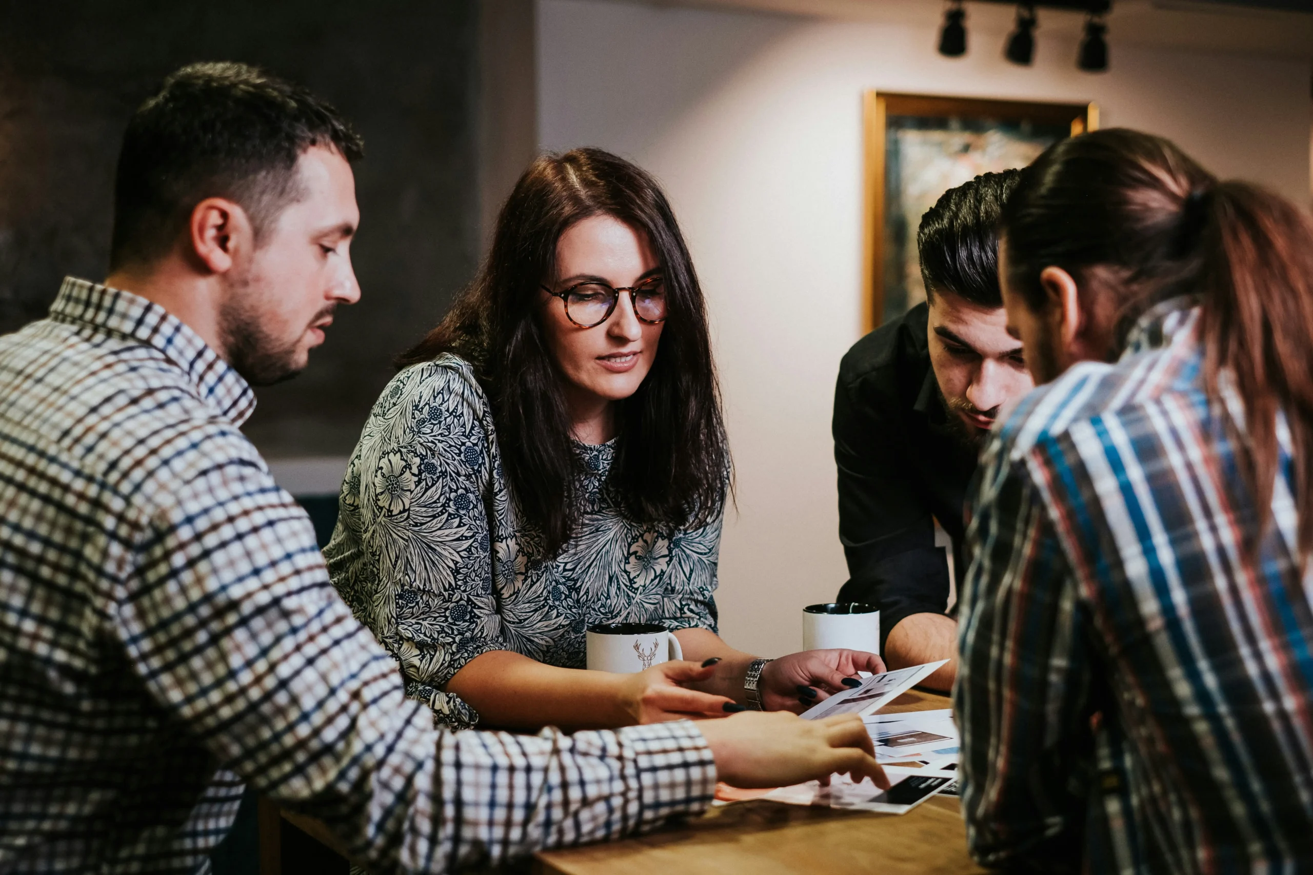 Four people surround a table looking at a pile of papers together.