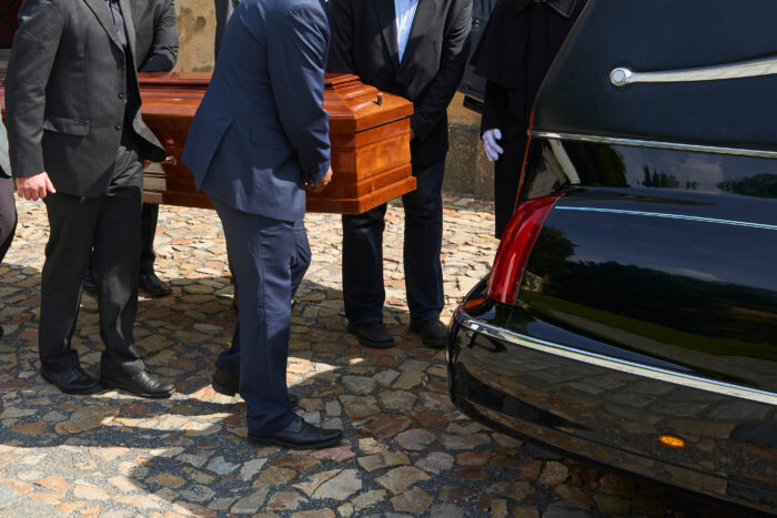 Coffin bearers load a coffin onto a hearse.