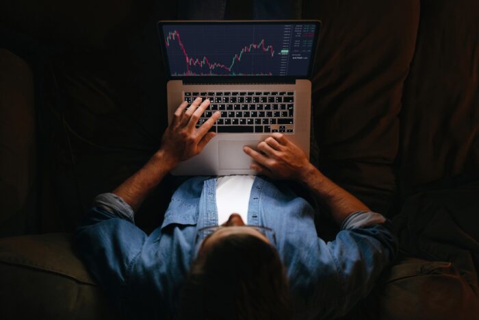 A man wearing glasses sits at a computer looking at data charts.
